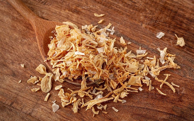 Smoked onion flakes, on a wooden spoon, wooden table, close-up