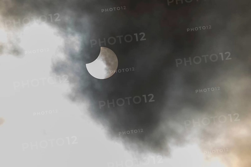 A partial solar eclipse occurs when the moon eclipses part of the sun and is surrounded by dynamic cloud formations. The event takes place during the day and offers an impressive visual experience. High Rhine, Vosges, Great East, France