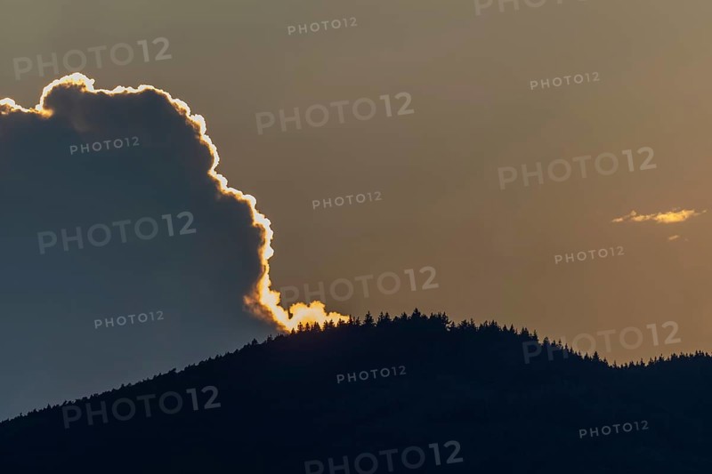 A radiant sunset conjures up warm colours as the clouds hang over a mountain range. Trees line the slopes and adorn the breathtaking sunset. The sky transitions to night. Bas rhin, Alsace, Grand Est, France