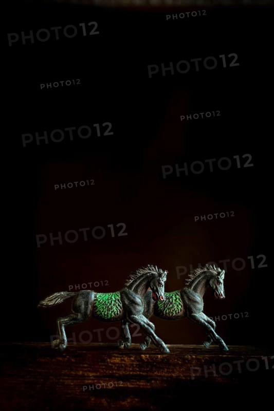 Two intricately designed horse figurines are positioned side by side, appearing to run forward. The dark background highlights their detailed feature