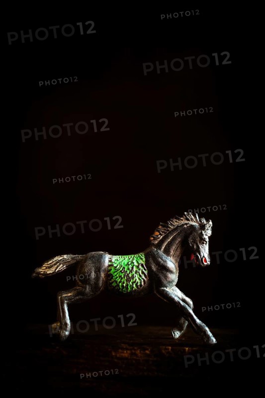 A black horse figurine is captured in mid-gallop, showcasing detailed green patterns on its side. The dark background enhances the vivid colors and highlights the horse's motion