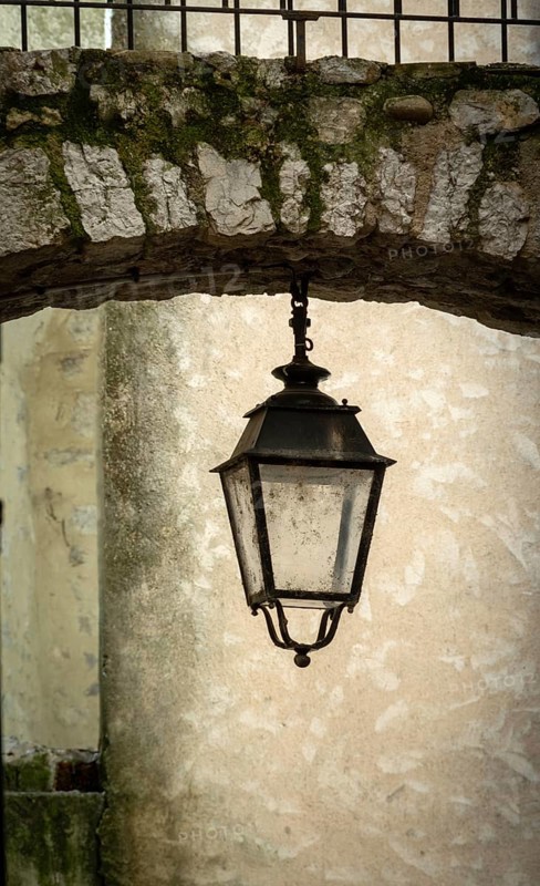Sisteron. A hanging lantern is positioned beneath an archway made of weathered stone. Alpes-de-Haute-Provence. Provence-Alpes-Côte d'Azur. France
