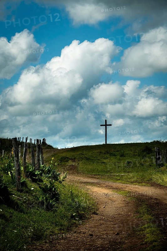 A winding dirt road leads the eye to a solitary cross. Cézallier, Auvergne Volcanoes Regional Natural Park, Puy-de-Dôme, Auvergne Rhone Alpes, France
