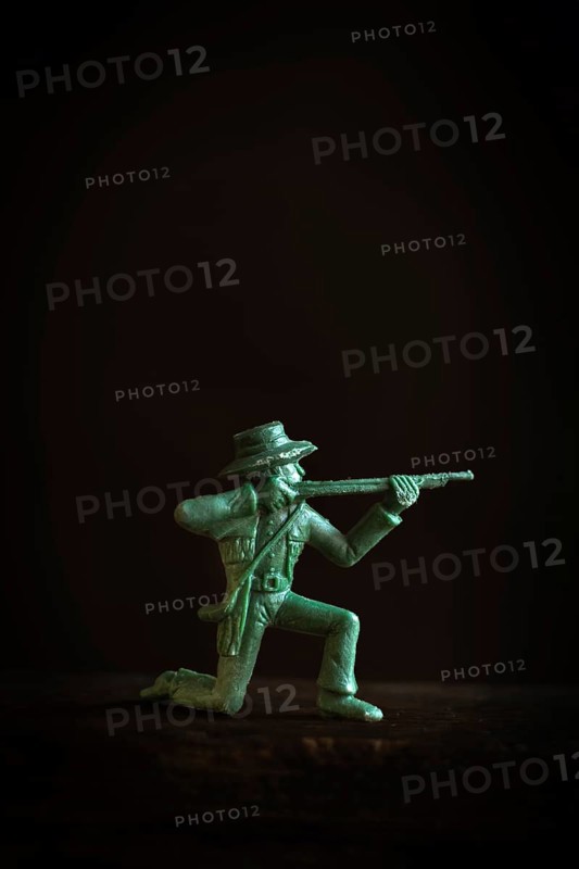 A detailed figurine of a gunslinger kneels and aims a rifle in a low light setting. Striking shadows enhance the figure's features, creating a tense and action-filled atmosphere