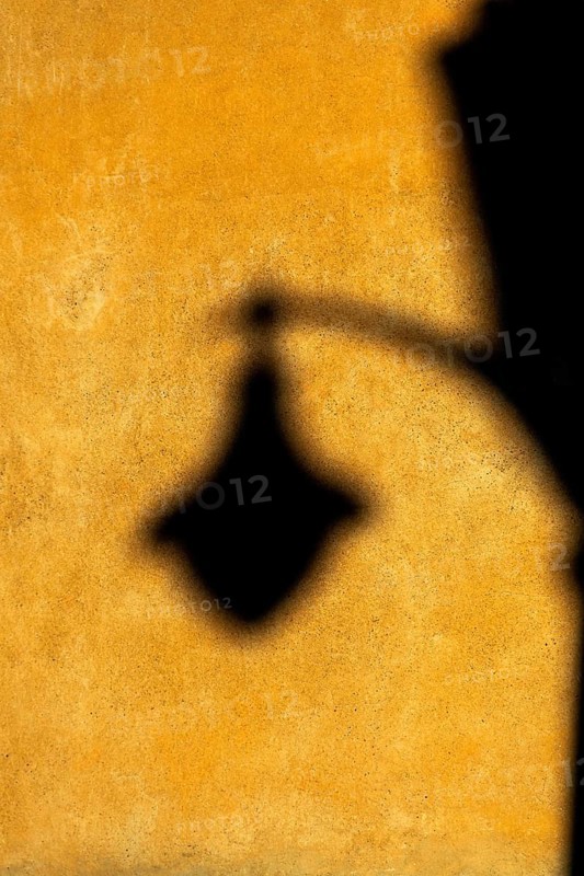 Soft afternoon light creates a striking shadow of a lantern on a textured yellow wall. The warm colors add depth, enhancing the tranquil atmosphere of the setting