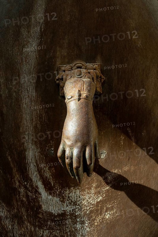 A decorative hand-shaped door knocker is firmly mounted on a weathered wooden door showcasing rich textures and an antique charm in a historic building