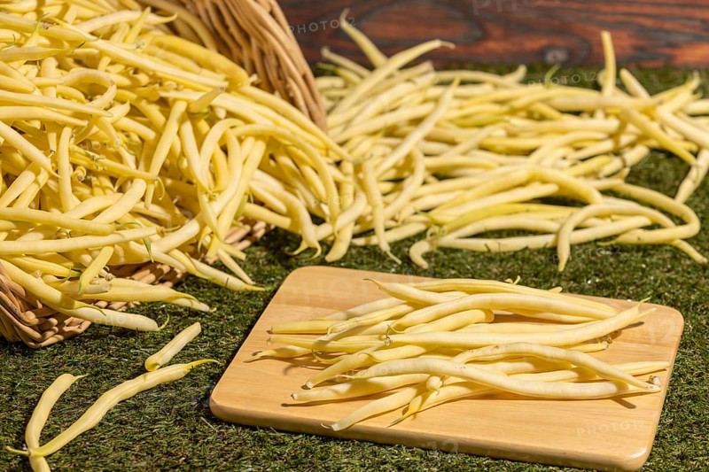 A basket of yellow beans, some on a board on a green background