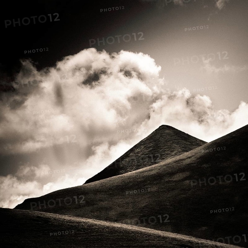 A striking view of a mountain peak stands tall against a backdrop of swirling clouds. Sancy Massif, Puy de Dome, Auvergne Rhone Alpes, France