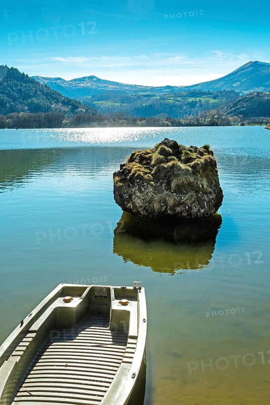 Lake chambon reflects the stunning blue sky and surrounding mountains. A small boat rests at the shore. Puy de Dome. Auvergne. France