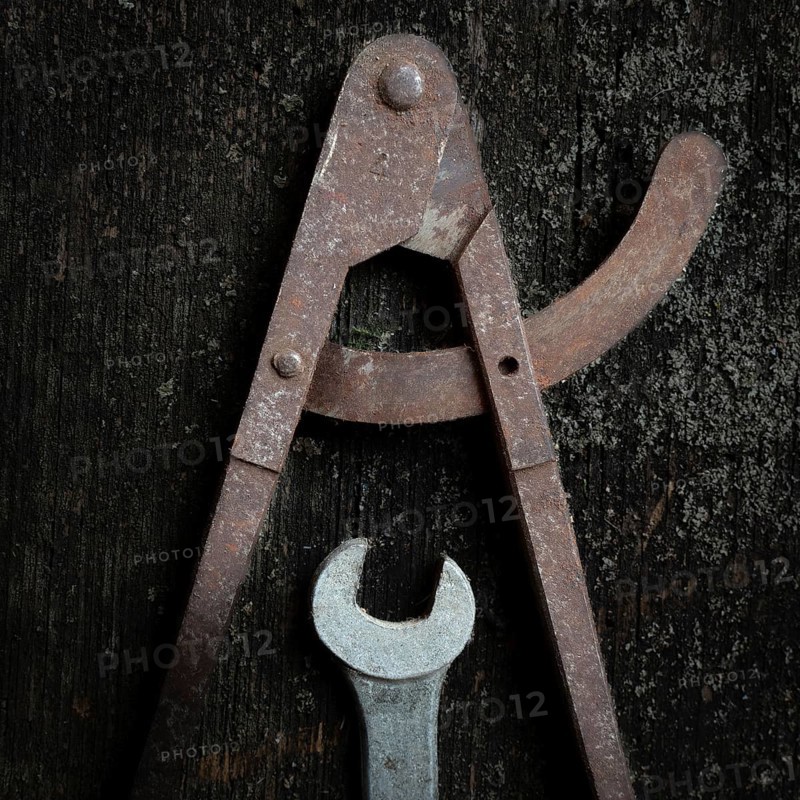 Two old metal tools, a caliper and adjustable wrench, lay on a textured wooden surface, revealing their wear and the beauty of traditional craftsmanship over time
