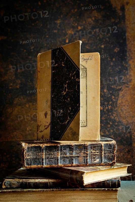 A collection of vintage books is displayed on a wooden table, accompanied by an old-fashioned notebook. The cozy dim lighting enhances the inviting ambiance, perfect for reading or writing