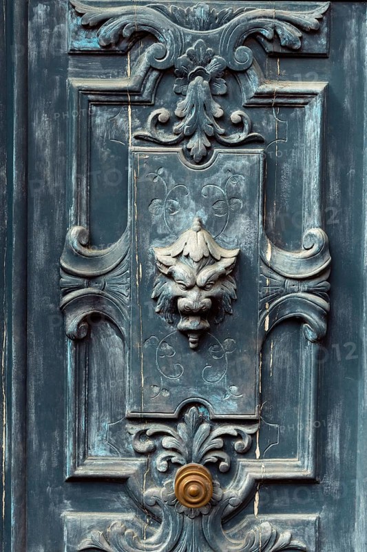 A striking door features detailed carvings and a lion head knocker, blending antique charm with wear marks that tell stories of a bygone era