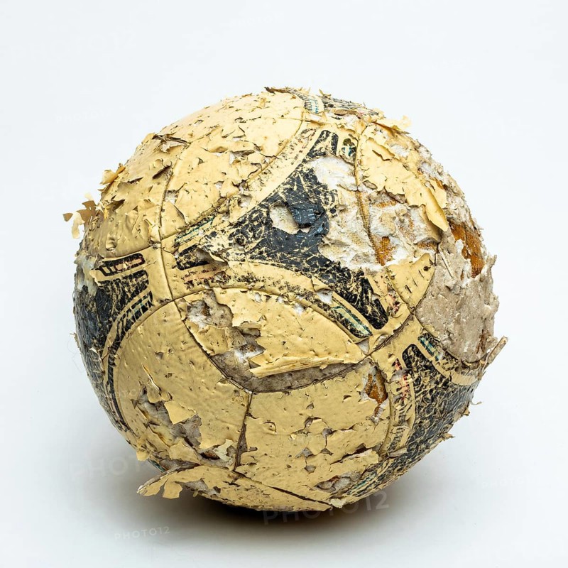 A worn football ball rests against a neutral background, displaying significant peeling and faded markings. The condition reflects years of use, capturing the essence of play and nostalgia