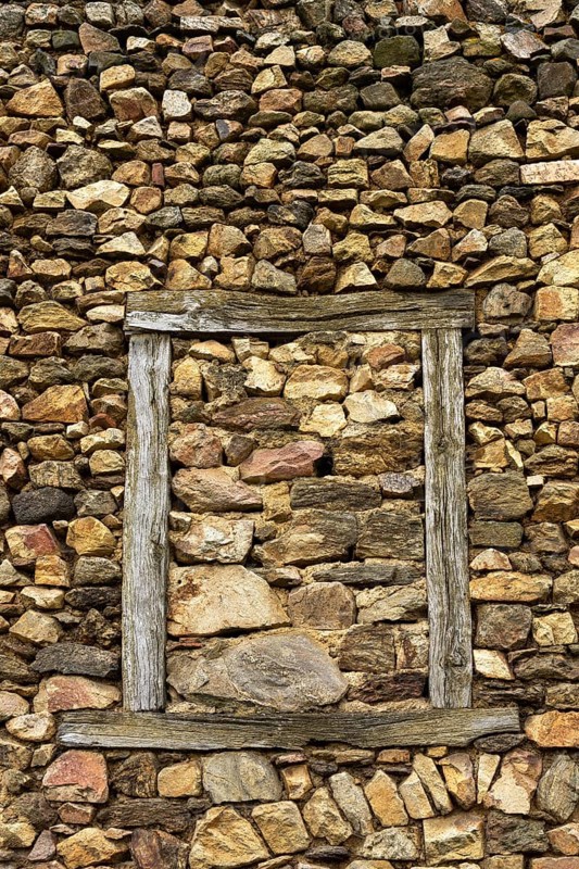 A wall constructed of unevenly arranged stones features a striking wooden frame that outlines an empty space where a window once existed, reflecting natural craftsmanship. France