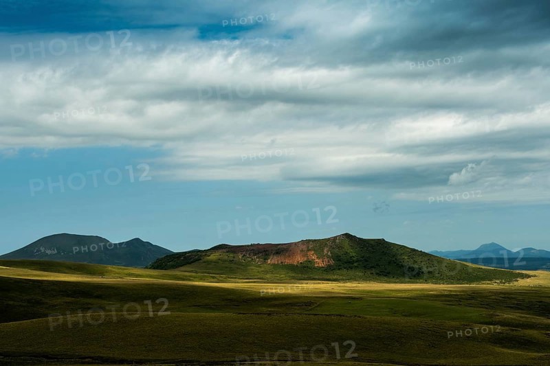 Mountains stretch across the landscape under a vast sky filled with dynamic clouds. Sancy Massif in Auvergne volcanoes Regional Natural Park. France