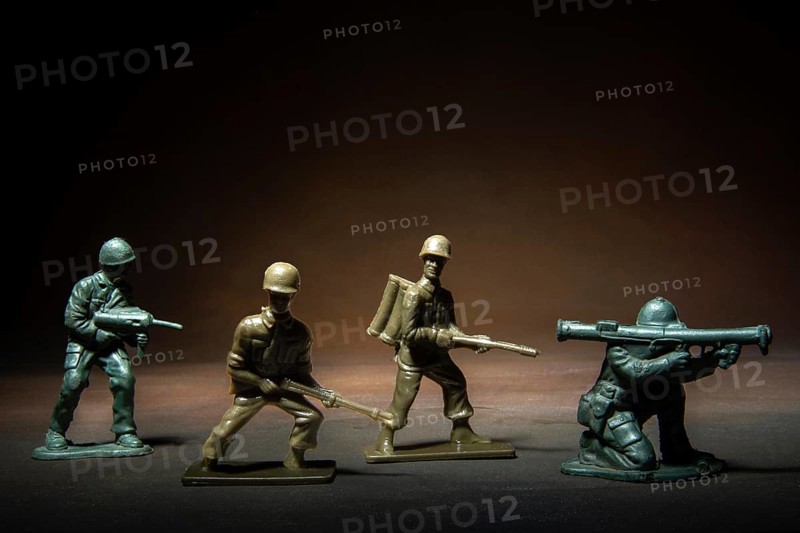 Four miniature soldier figures positioned in a tense standoff, showcasing various combat stances illuminated by a soft, dramatic light against a dark background