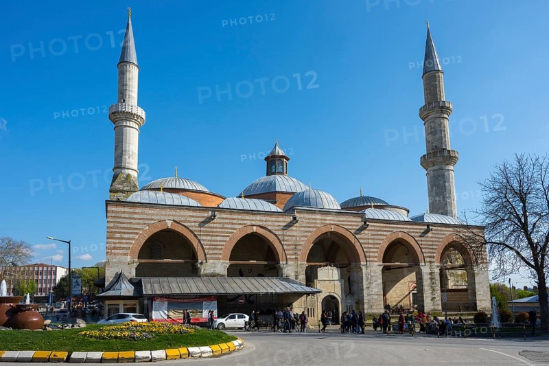 Historic mosque with two minarets on a busy street. The sky is sunny with clear blue. Old Mosque, Eski Camii, Edirne, Eastern Thrace, Turkey