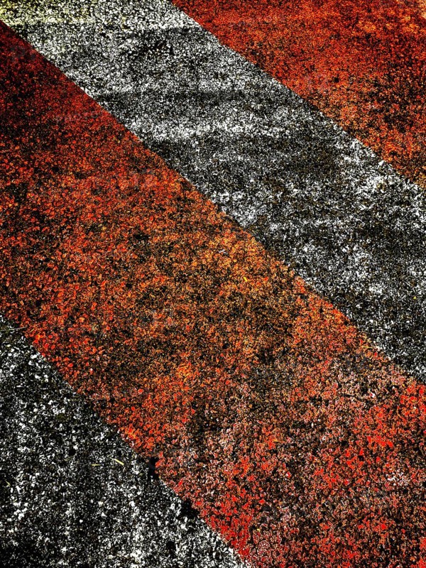 Bold red and black lines create an eye-catching pattern on a rough surface, illuminated by warm late afternoon light, showcasing texture and color contrast effectively