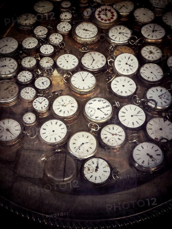 A variety of vintage pocket watches are arranged neatly on a reflective surface in an antique shop, showcasing diverse styles and intricate details that capture the essence of craftsmanship
