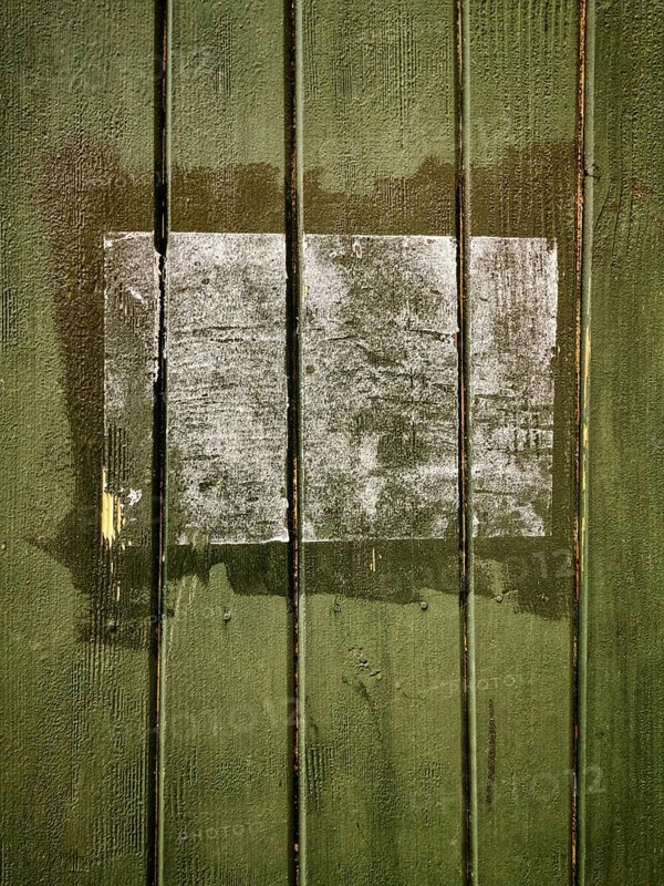 A rectangular patch on a green wooden surface shows faded remnants of a past application, with chipped paint revealing the wood grain. The area indicates age and neglect