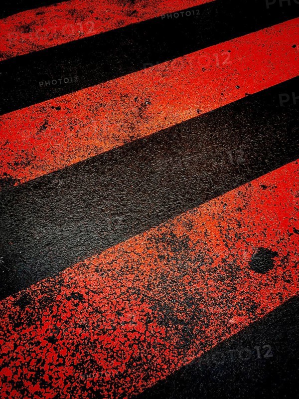 A vibrant red and black striped crosswalk painted across the asphalt. The surface shows signs of wear, indicating heavy pedestrian use in an urban environment