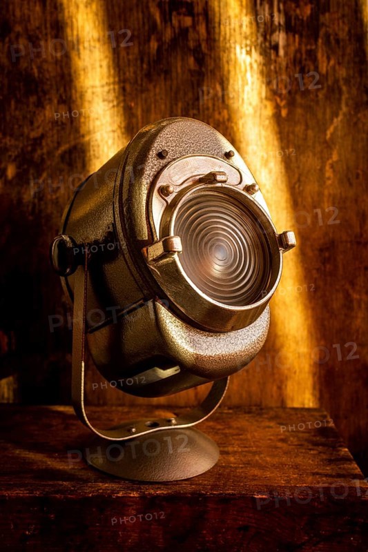 A vintage spotlight rests on a rustic wooden surface, casting a warm glow. Soft light enhances the aged texture of the wood, creating a nostalgic atmosphere