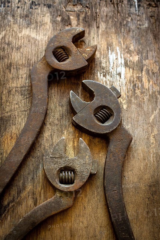 Three antique adjustable wrenches rest on a weathered wooden table, highlighting their unique designs and sturdy construction. They reflect the tools' historical significance in mechanics