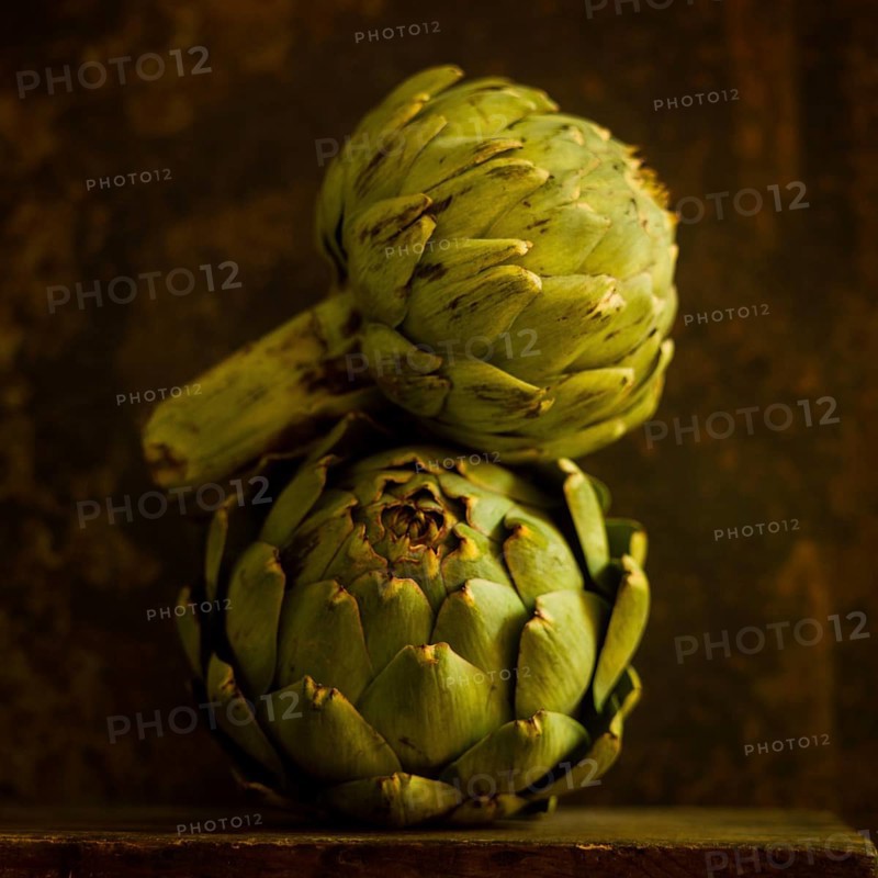 Two artichokes are prominently positioned against a rich brown background, highlighting their distinct shapes and textured surfaces, emphasizing natural beauty