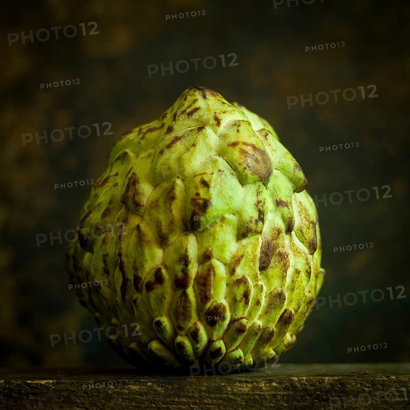 The sugar apple, known as annona squamosa, showcases its unique, scaly green exterior. This exotic fruit is placed on a rustic wooden surface, highlighting its distinct texture and features