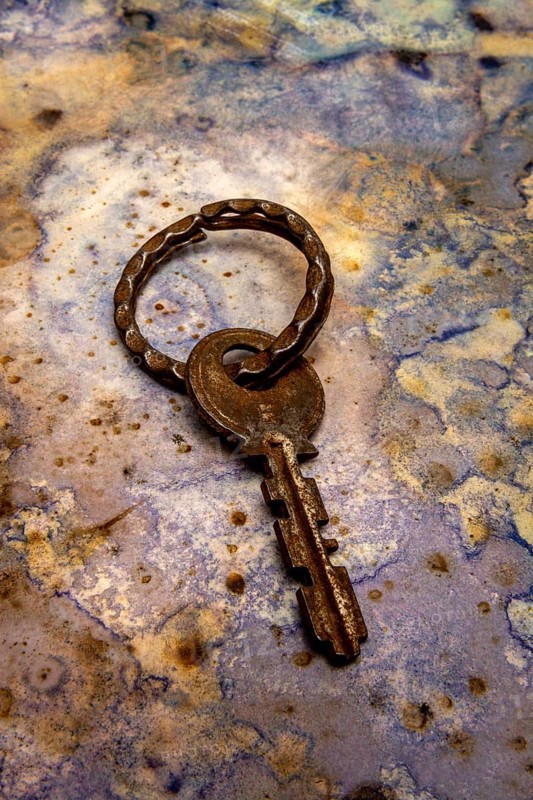 An aged key lies on a beautifully textured surface, showcasing its unique design and patina. The earthy tones highlight the key's vintage character, evoking stories from the past