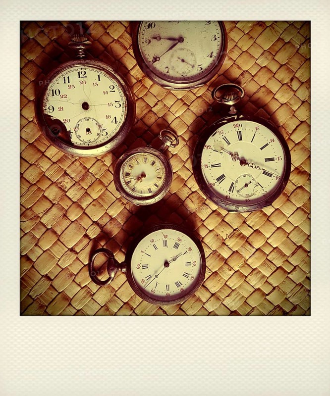 Various vintage stopwatches are displayed closely on a woven surface, highlighting their distinct designs, aged patinas, and intricate dials