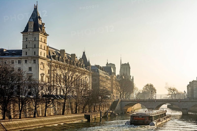 A tour boat navigates the flowing waters of the River Seine, revealing the stunning architecture of Quai des Orfevres and Palais de Justice under a clear sky. Paris. France