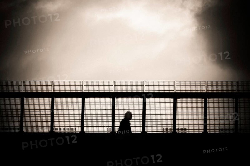 A solitary figure walks along a metal gangway in Lausanne, Switzerland, with a dramatic cloudy sky in the background, capturing a moment of reflection and solitude during late afternoon