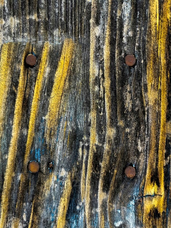 Detailed close-up shows an aged wooden surface featuring unique yellow streaks and rusty nails. The texture reflects natural aging and weathering processes over time