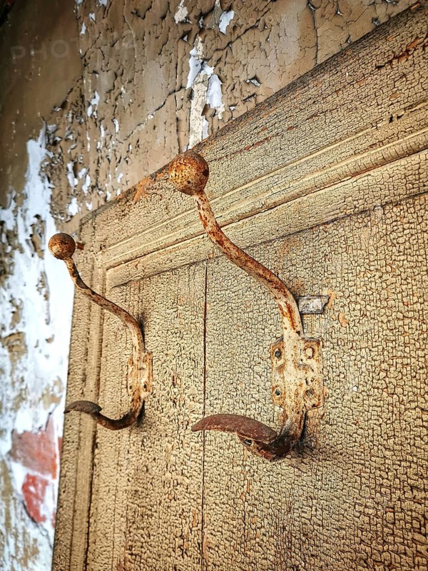 Rusty hooks attached to a weathered wall in a dilapidated building showcasing decay and abandonment