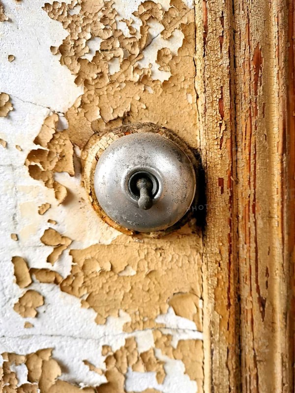 Close view of a keyhole on a weathered, peeling door demonstrates intricate details and textures. The contrast of the metallic keyhole against the aged surface speaks to its history