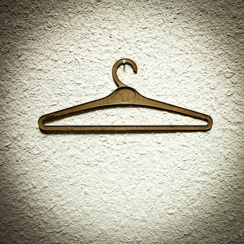 A clothes hanger is suspended from a textured wall, showcasing a minimalist design. The simple indoor setting allows the focus to remain on the hanger, illuminated by natural light