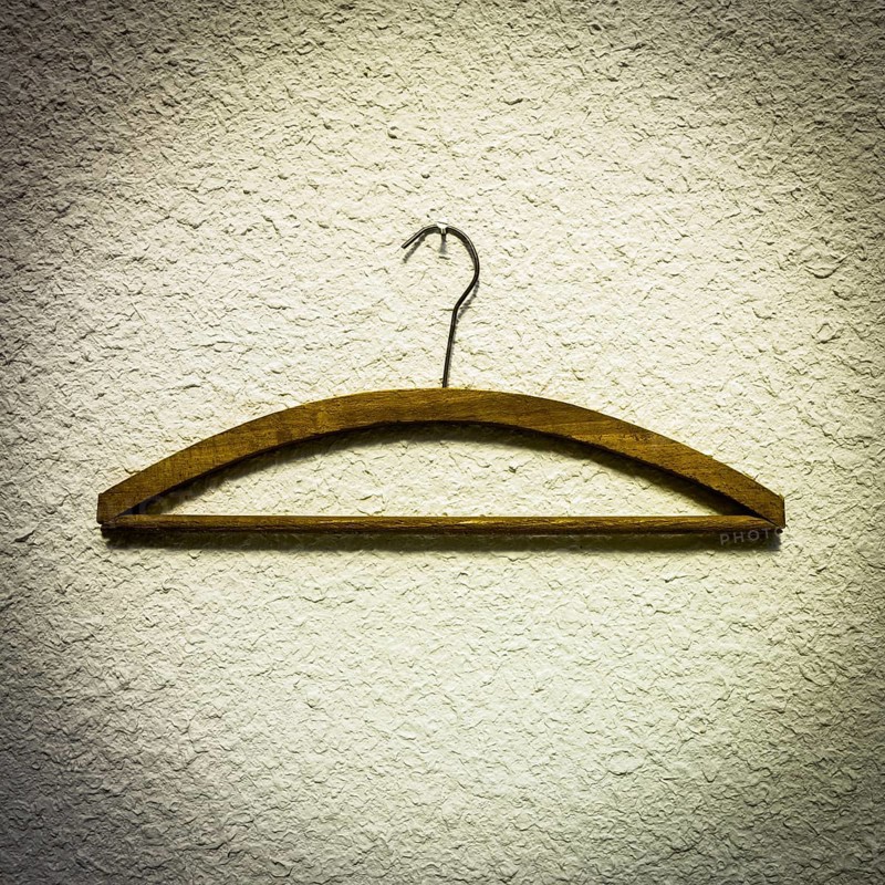 Wooden hangers are displayed against a textured light wall, highlighting a minimalist approach to clothing organization in an indoor closet area, suitable for modern decor