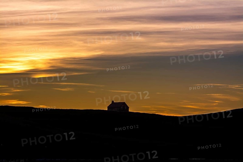 A tranquil farm stands silhouetted against the colorful sky at sunset, showcasing the natural beauty of the Cezallier massif in the Regional Nature Park of Volcans d'Auvergne, Puy de Dome, Auvergne Rhone Alpes, France