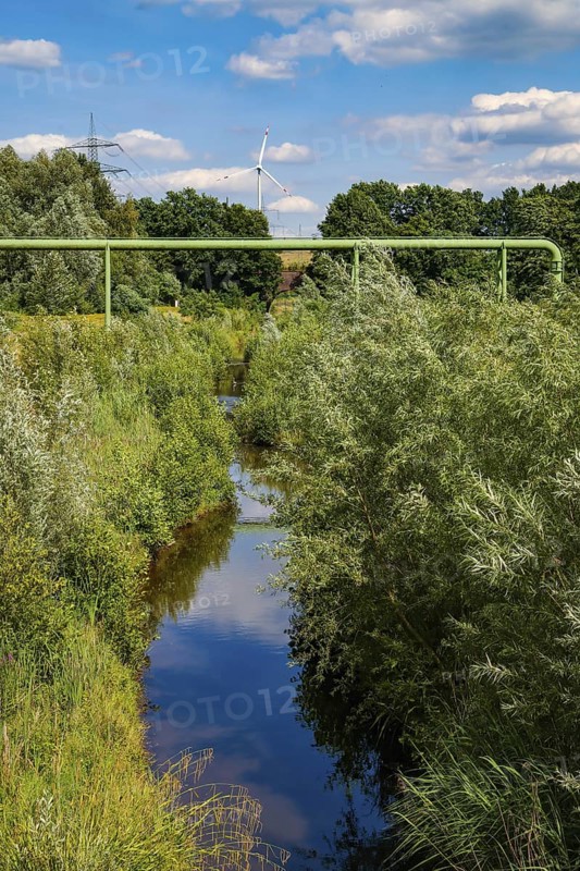 Bottrop, North Rhine-Westphalia, Germany - Renaturalised Boye, the tributary of the Emscher, has been transformed into a near-natural watercourse, flood protection through newly designed flooding areas, the Boye is now free of wastewater following the construction of a parallel sewer, is part of the Emscher river system and thus part of the Emscher conversion, was previously an open, above-ground wastewater channel, mixed water channel with surface water and wastewater. Wind turbine on the Mottbruch spoil tip at the back