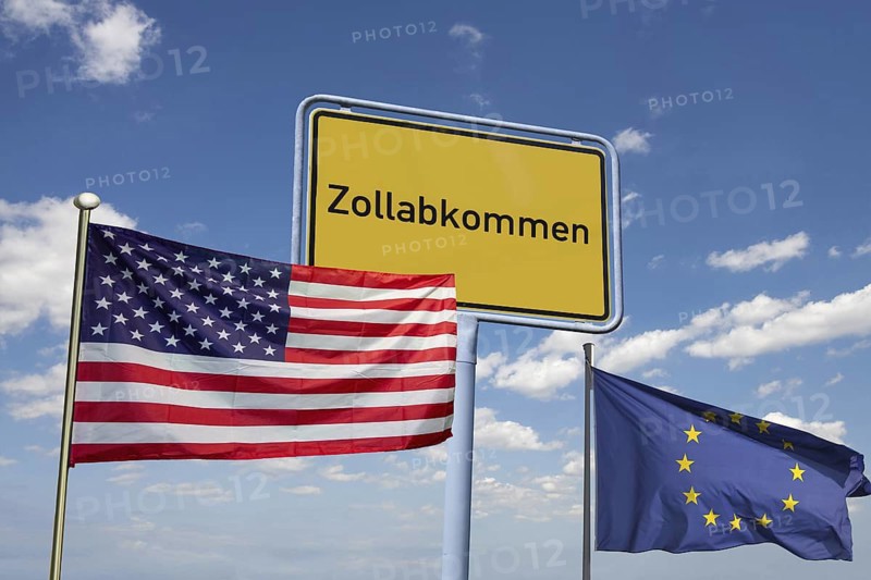 (Photomontage) Symbolic image of the customs agreement between the EU and the USA: town sign with the inscription ZOLLABKOMMEN with American and European flags against a blue sky