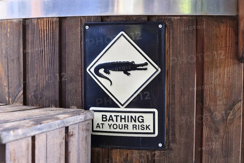Warning sign Bathing at your risk with alligator symbol on wooden hot tub. Humorous caution notice for bathers