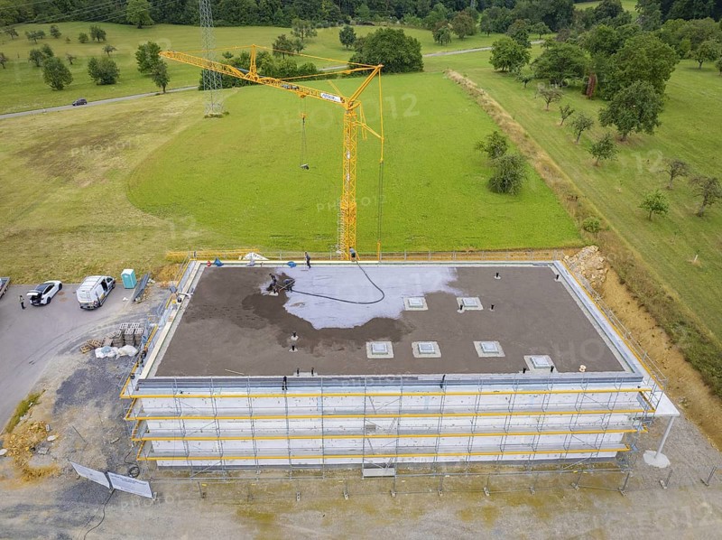 Drone shot of a construction site with crane and partially constructed building on a large green area, green roof, house construction, climate neutral