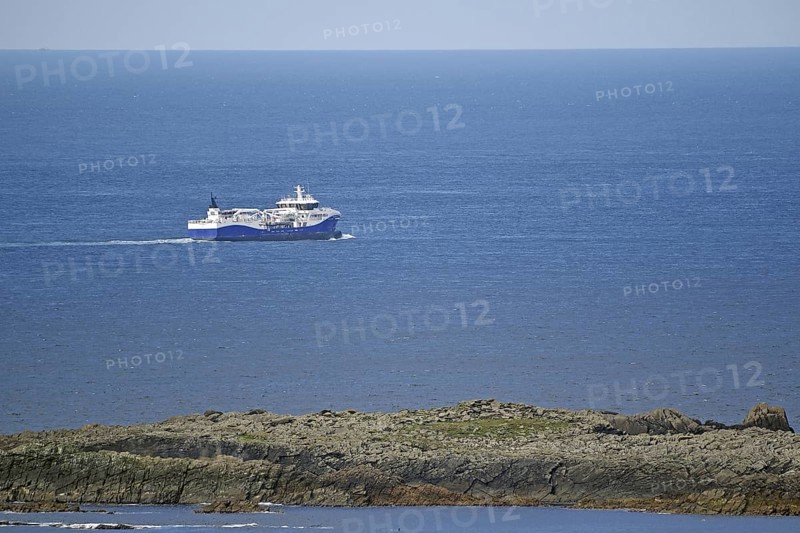 A large fishing vessel navigates the blue sea along the rocky coastline, Sumburgh Head, Shetland Islands, Scotland, United Kingdom