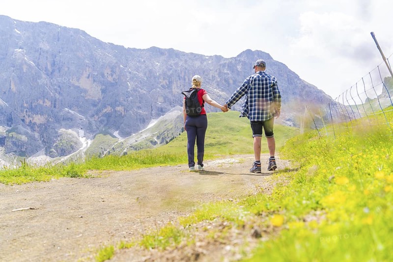 Couple holding hands and walking on a mountain path on a sunny day, Alpe di Siusi, Dolomites, South Tyrol, Italy