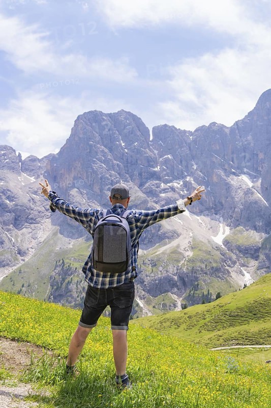 A hiker stands with outstretched arms in front of a mountain backdrop on a green meadow, Alpe di Siusi, Dolomites, South Tyrol, Italy