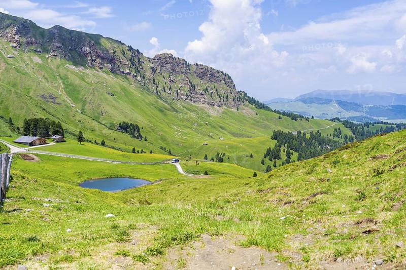 View of a wide mountain landscape with a small lake and green hills under a cloudy sky, Alpe di Siusi, Dolomites, South Tyrol, Italy