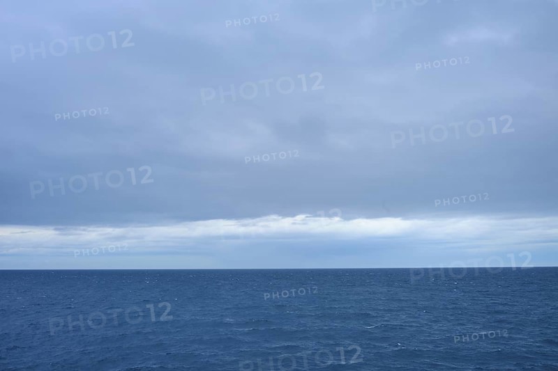 A calm sea stretches to the horizon with thick clouds in the sky, summer, Cook Strait, North Island, South Island, New Zealand