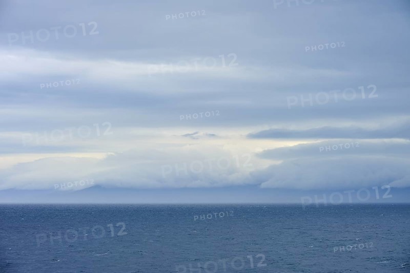 Calm sea under a dense canopy of clouds, mountains visible in the distance, summer, Cook Strait, North Island, South Island, New Zealand