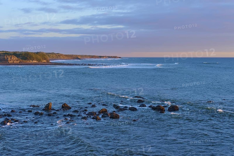Rocks in the sea under a pink-orange sky at sunset, summer, Opunake, Taranaki, North Island, New Zealand